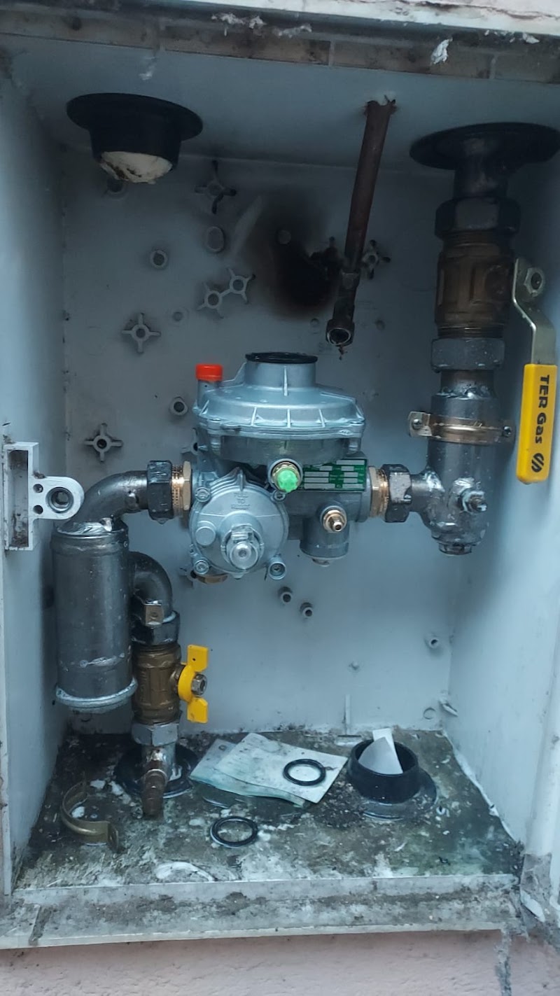 Armario de gas abierto con el regulador y el filtro montados, la llave general con maneta amarilla a la derecha y los restos de obra en el fondo.